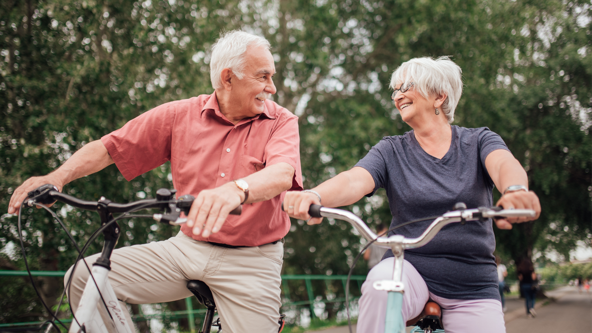 Two older individuals riding their bikes and smiling at each other