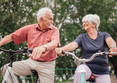 Two older individuals riding their bikes and smiling at each other